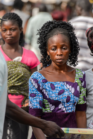 LOME, TOGO - Jan 9, 2017: Unidentified Togolese woman in colored dress looks down at the Lome central market. Togo people suffer of poverty due to the bad economyのeditorial素材