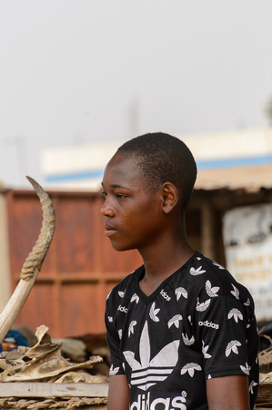 LOME, TOGO - Jan 9, 2017: Unidentified Togolese boy in adidas shirt looks away at the Lome fetish market. Togo people suffer of poverty due to the bad economyのeditorial素材