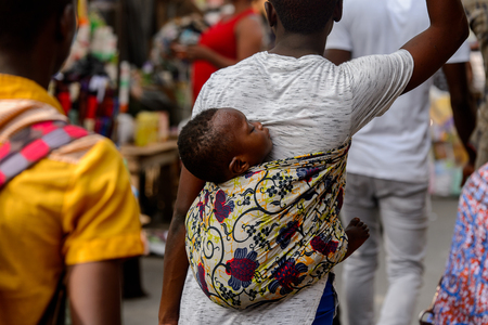 LOME, TOGO - Jan 9, 2017: Unidentified Togolese baby boy carried by his parent on his back at the Lome central market. Togo children suffer of poverty due to the bad economyのeditorial素材