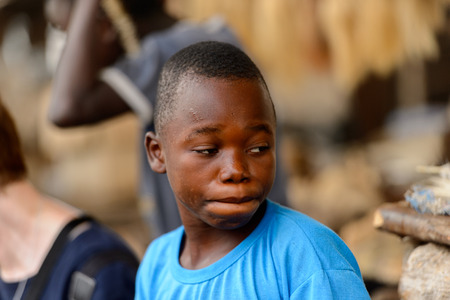 LOME, TOGO - Jan 9, 2017: Unidentified Togolese boy in blue shirt hides his lips at the Lome fetish market. Togo children suffer of poverty due to the bad economyのeditorial素材