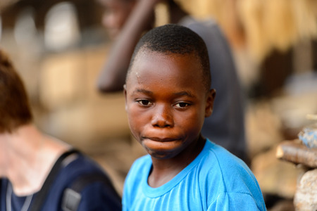 LOME, TOGO - Jan 9, 2017: Unidentified Togolese boy in blue shirt hides his lips at the Lome fetish market. Togo children suffer of poverty due to the bad economyのeditorial素材