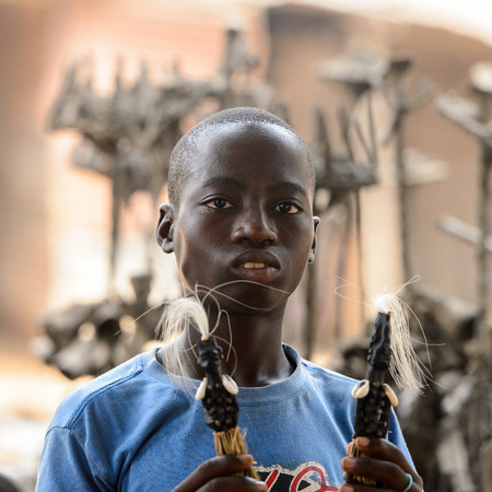 LOME, TOGO - Jan 9, 2017: Unidentified Togolese young boy holds a couple of figures to sell at the Lome fetish market. Togo people suffer of poverty due to the bad economyのeditorial素材