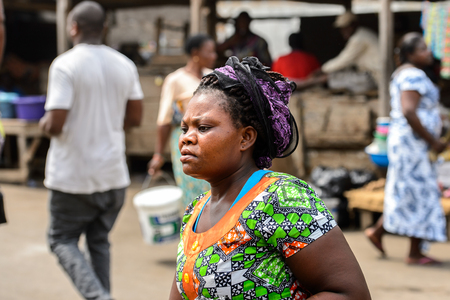 LOME, TOGO - Jan 9, 2017: Unidentified Togolese woman in colored shirt and braids walks at the Lome port. Togo people suffer of poverty due to the bad economyのeditorial素材