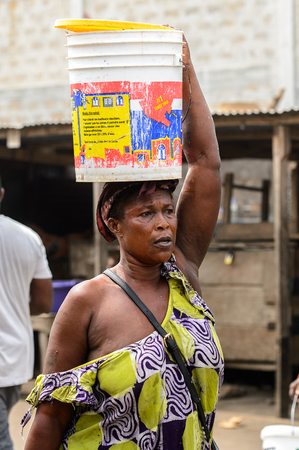 LOME, TOGO - Jan 9, 2017: Unidentified Togolese woman carries a couple of buckets on her head at the Lome port. Togo people suffer of poverty due to the bad economyのeditorial素材