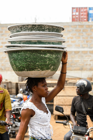 LOME, TOGO - Jan 9, 2017: Unidentified Togolese woman carries couple of basins on her head at the Lome port. Togo people suffer of poverty due to the bad economyのeditorial素材