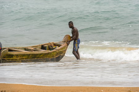 LOME, TOGO - Jan 9, 2017: Unidentified Togolese man stands in water near the boat on the coast of the Gulf of Guinea. Togo people suffer of poverty due to the bad economyのeditorial素材