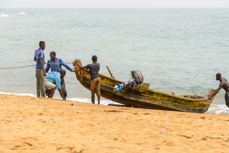 LOME, TOGO - Jan 9, 2017: Unidentified Togolese men pull a boat out of water on the coast of the Gulf of Guinea. Togo people suffer of poverty due to the bad economyのeditorial素材