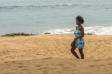LOME, TOGO - Jan 9, 2017: Unidentified Togolese beautiful woman in colored dress walks on the coast of the Gulf of Guinea. Togo people suffer of poverty due to the bad economyのeditorial素材