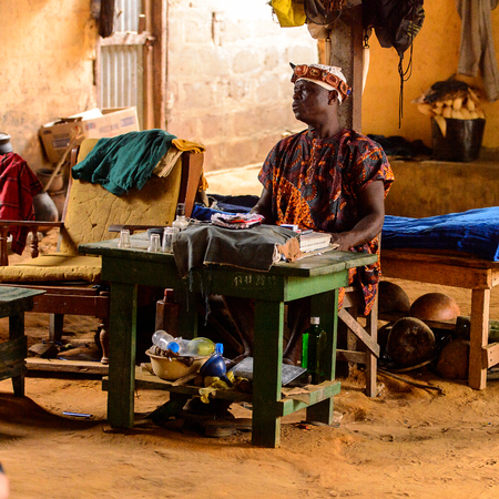 LOME, TOGO - Jan 9, 2017: Unidentified Togolese local shaman sits by the table in his house. Togo people suffer of poverty due to the bad economyのeditorial素材