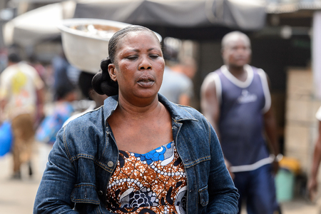 LOME, TOGO - Jan 9, 2017: Unidentified Togolese woman in colored shirt and a jacket walks at the Lome port. Togo people suffer of poverty due to the bad economyのeditorial素材