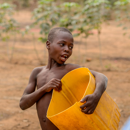 LOME, TOGO - Jan 9, 2017: Unidentified Togolese young boy holds yellow bucket. Togo children suffer of poverty due to the bad economyのeditorial素材