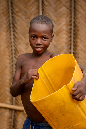 LOME, TOGO - Jan 9, 2017: Unidentified Togolese young boy holds yellow bucket. Togo children suffer of poverty due to the bad economyのeditorial素材