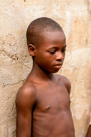 LOME, TOGO - Jan 9, 2017: Unidentified Togolese young boy leans on the wall of the local shaman's house. Togo children suffer of poverty due to the bad economyのeditorial素材