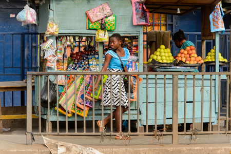 ACCRA, GHANA - Jan 8, 2017: Unidentified Ghanaian girl passes by shop and looks around. People of Ghana suffer of poverty due to the economic situationのeditorial素材