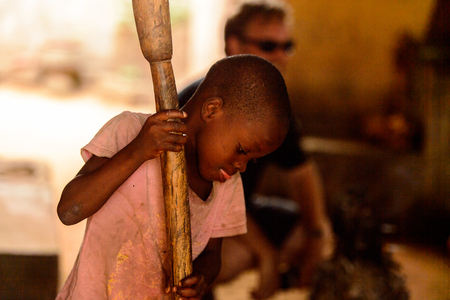 LOME, TOGO - Jan 9, 2017: Unidentified Togolese young boy holds a wooden stick in the local shaman's house. Togo children suffer of poverty due to the bad economyのeditorial素材