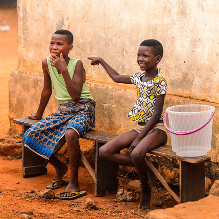 OUIDAH, BENIN - Jan 9, 2017: Unidentified Beninese girls sit on the wooden bench on the street. Benin people suffer of poverty due to the bad economyのeditorial素材