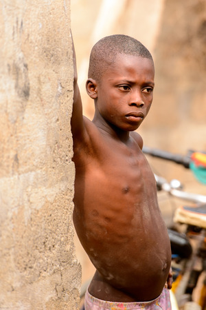 LOME, TOGO - Jan 9, 2017: Unidentified Togolese young boy leans on the wall of the local shaman's house. Togo children suffer of poverty due to the bad economyのeditorial素材