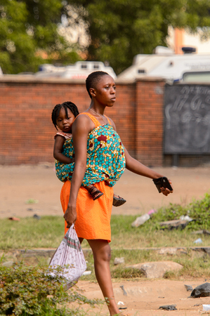 ACCRA, GHANA - Jan 8, 2017: Unidentified Ghanaian woman  carries her baby on her back on the street. People of Ghana suffer of poverty due to the economic situationのeditorial素材