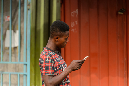 ACCRA, GHANA - Jan 8, 2017: Unidentified Ghanaian young man holds his cellphone in his hand. People of Ghana suffer of poverty due to the economic situationのeditorial素材