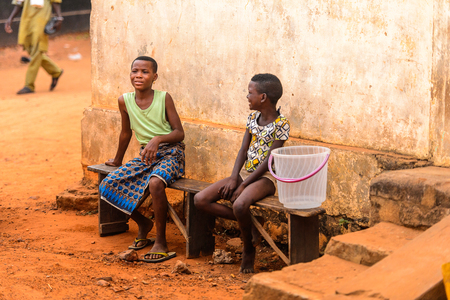 OUIDAH, BENIN - Jan 9, 2017: Unidentified Beninese girls sit on the wooden bench on the street. Benin people suffer of poverty due to the bad economyのeditorial素材