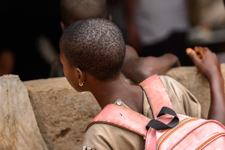LOME, TOGO - Jan 9, 2017: Unidentified Togolese young girl carries a backpack near the local shaman's house. Togo people suffer of poverty due to the bad economyのeditorial素材