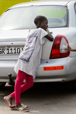 ACCRA, GHANA - Jan 8, 2017: Unidentified Ghanaian little girl leans on the car on the street. People of Ghana suffer of poverty due to the economic situationのeditorial素材