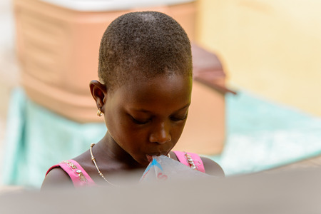 ACCRA, GHANA - Jan 8, 2017: Unidentified Ghanaian girl drinks water at the local market. People of Ghana suffer of poverty due to the economic situationのeditorial素材