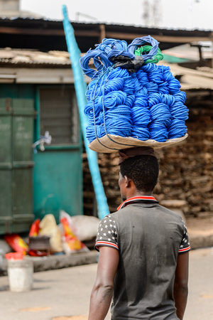 ACCRA, GHANA - Jan 8, 2017: Unidentified Ghanaian man carries a tray with ropes at the local market. People of Ghana suffer of poverty due to the economic situationのeditorial素材
