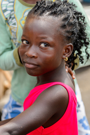 ACCRA, GHANA - Jan 8, 2017: Unidentified Ghanaian young girl in red shirt with curly hair at the local market. People of Ghana suffer of poverty due to the economic situationのeditorial素材