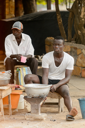 LOME, TOGO - Jan 9, 2017: Unidentified Togolese men in white shirts sit on wooden chairs near basins. Togo people suffer of poverty due to the bad economyのeditorial素材