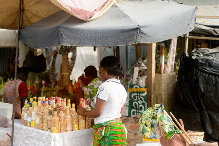 LOME, TOGO - Jan 9, 2017: Unidentified Togolese woman in white shirt and colored skirt sells bottles with nuts. Togo people suffer of poverty due to the bad economyのeditorial素材