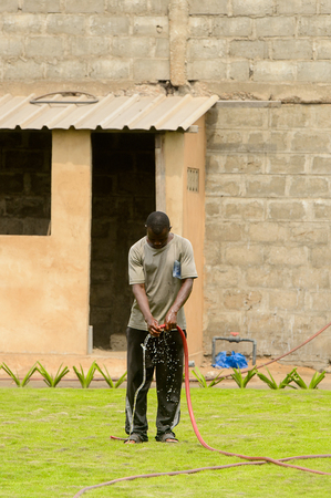 LOME, TOGO - Jan 9, 2017: Unidentified Togolese man waters the green lawn. Togo people suffer of poverty due to the bad economyのeditorial素材