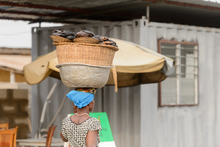 LOME, TOGO - Jan 9, 2017: Unidentified Togolese woman carries a basin on her head. Togo people suffer of poverty due to the bad economyのeditorial素材