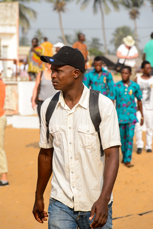 OUIDAH, BENIN - Jan 10, 2017: Unidentified Beninese man in shirt and a cap carries backpack at the voodoo festival, which is anually celebrated on January, 10th.のeditorial素材