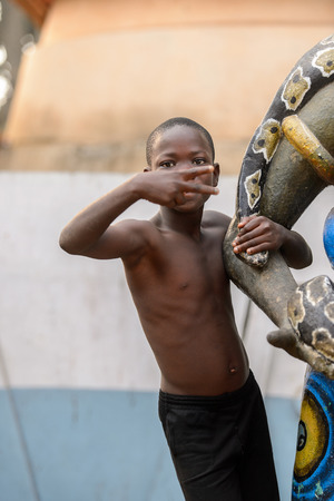 OUIDAH, BENIN - Jan 10, 2017: Unidentified Beninese  little boy holds on the statue and shows two fingers at the voodoo festival, which is anually celebrated on January, 10th.のeditorial素材