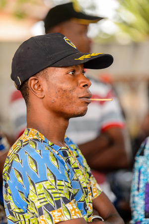 OUIDAH, BENIN - Jan 10, 2017: Unidentified Beninese man in shirt and a cap holds a wooden stick in his mouth at the voodoo festival, which is anually celebrated on January, 10th.のeditorial素材