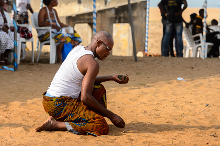 OUIDAH, BENIN - Jan 10, 2017: Unidentified Beninese man in colored clothes collects something in sand at the voodoo festival, which is anually celebrated on January, 10th.のeditorial素材