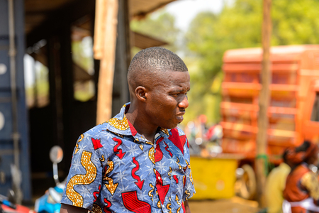 OUIDAH, BENIN - Jan 10, 2017: Unidentified Beninese man in colored shirt frowns at the local market. Benin people suffer of poverty due to the bad economyのeditorial素材