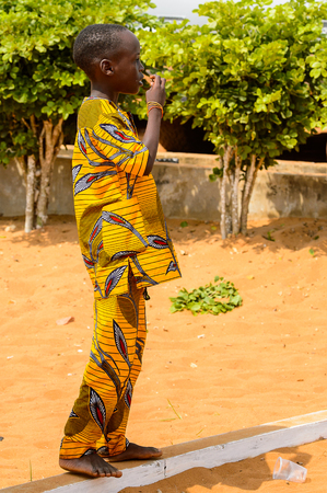 OUIDAH, BENIN - Jan 10, 2017: Unidentified Beninese  little boy in yellow suit stands at the voodoo festival, which is anually celebrated on January, 10th.のeditorial素材