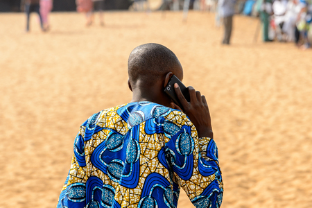 OUIDAH, BENIN - Jan 10, 2017: Unidentified Beninese boy in colored clothes talks on the phone at the voodoo festival, which is anually celebrated on January, 10th.のeditorial素材