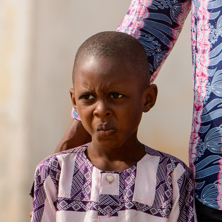 OUIDAH, BENIN - Jan 10, 2017: Unidentified Beninese little boy wears suit in stripes and grimaces at the voodoo festival, which is anually celebrated on January, 10th.のeditorial素材