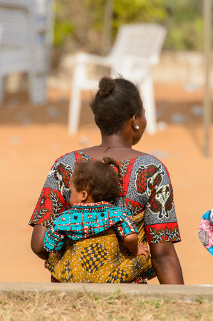 OUIDAH, BENIN - Jan 10, 2017: Unidentified Beninese woman in colored dress carries a baby at the voodoo festival, which is anually celebrated on January, 10th.のeditorial素材