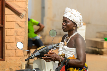 OUIDAH, BENIN - Jan 10, 2017: Unidentified Beninese woman in white headscarf and colored clothes on the street. Benin people suffer of poverty due to the bad economyのeditorial素材