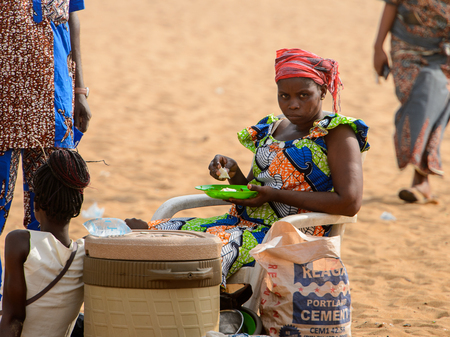 OUIDAH, BENIN - Jan 10, 2017: Unidentified Beninese woman in colored clothes eats at the voodoo...