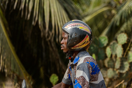 OUIDAH, BENIN - Jan 10, 2017: Unidentified Beninese man in helmet rides a motocycle in colored...