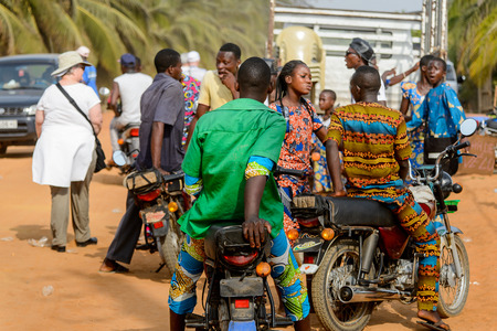 OUIDAH, BENIN - Jan 10, 2017: Unidentified Beninese group of people sit on the motocycles on the street from behind. Benin people suffer of poverty due to the bad economyのeditorial素材