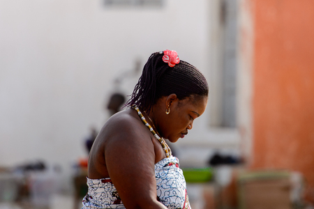 OUIDAH, BENIN - Jan 10, 2017: Unidentified Beninese woman in colored clothes with braids looks down. Benin people suffer of poverty due to the bad economyのeditorial素材