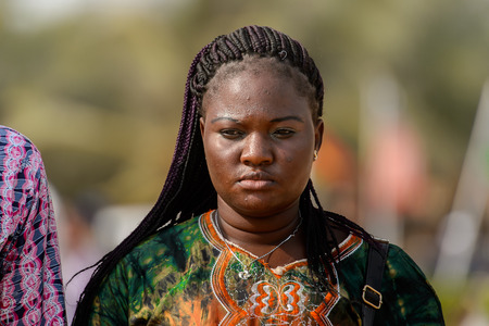 OUIDAH, BENIN - Jan 10, 2017: Unidentified Beninese woman with braids in colored clothes at the...