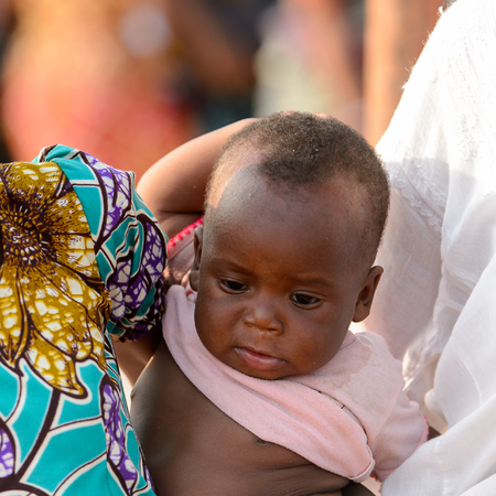 OUIDAH, BENIN - Jan 10, 2017: Unidentified Beninese little baby in pink shirt looks down at the local market. Benin children suffer of poverty due to the bad economyのeditorial素材
