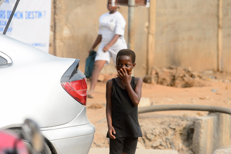 OUIDAH, BENIN - Jan 10, 2017: Unidentified Beninese boy in black shirt covers his face with his hand on the street. Benin people suffer of poverty due to the bad economyのeditorial素材